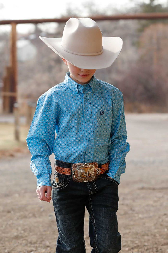 Little boy wearing light blue geo print Cinch long sleeve shirt. He is also wearing a silver belly cowboy hat, jeans, and a belt. Front view.