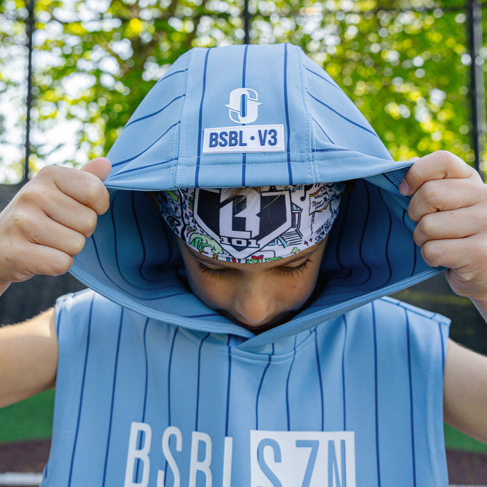 Youth player pulling up the hood of the light blue pinstripe BSBL-SZN Short Sleeve Hoodie V3, showing the Jackson Olson "O" logo and "BSBL·V3" label with the graphic headband visible underneath