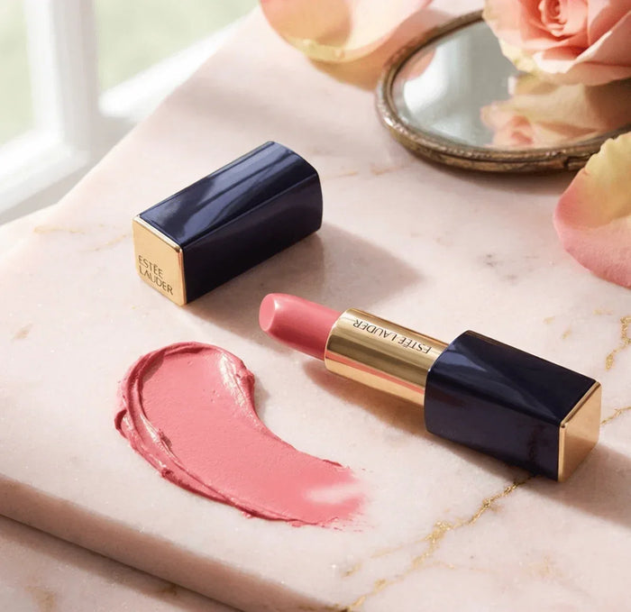 Matte pink lipstick with gold and navy case on marble beside pink rose and mirror