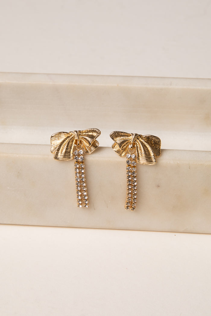 Gold bow-shaped earrings on a marble surface