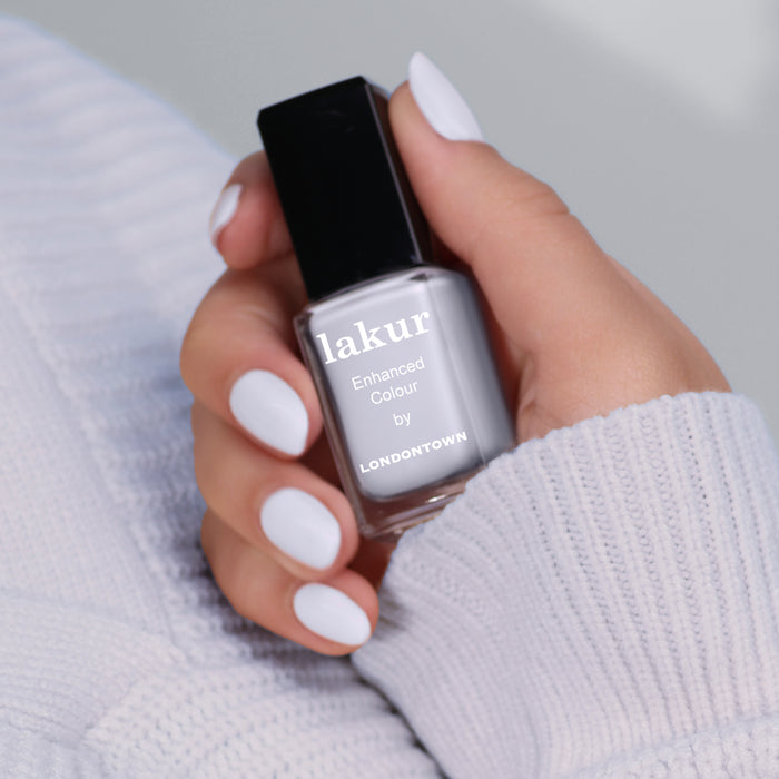 A hand holding a bottle of "Frostbitten by LONDONTOWN" nail polish with nails painted in an icy blue shade.