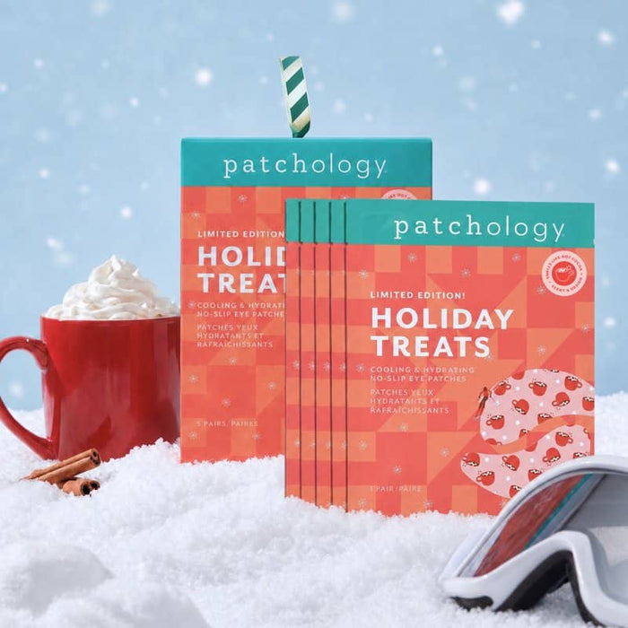 Holiday eye masks boxes standing in a snowy setup with a red mug of whipped cream, cinnamon sticks, and ski goggles on a blue snowy background.