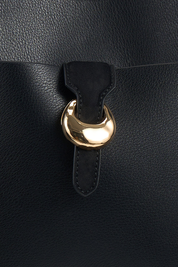 Close up shot of the molten metal Signature Cannon Street clap closure on the front pocket on the Lilibet Black faux leather Laptop Tote