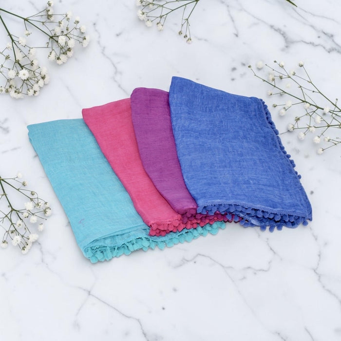 Four colorful scarves stacked on a marble surface with baby's breath flowers.