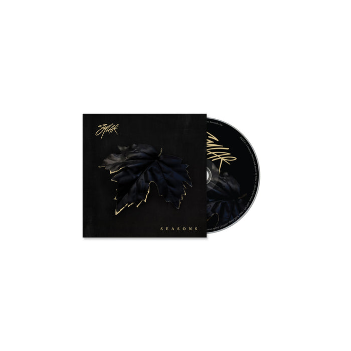 The Sylar CD and case have a black background with a dark, gold-outlined leaf in the center. SEASONS, inspired by tracks like Open Wounds, and Sylarβs stylized signature are displayed in shimmering gold lettering.