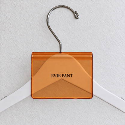 Orange transparent acrylic hanger sign clip with soft edge reflections, resting on a white wooden hanger, with example EVIE PANT print