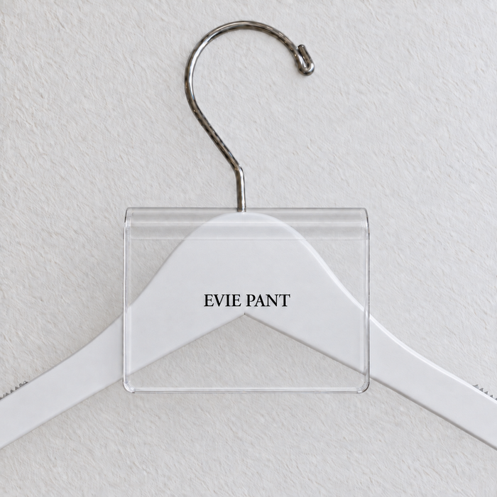 Clear acrylic hanger sign clip with soft edge reflections, resting on a white wooden hanger, with example EVIE PANT print