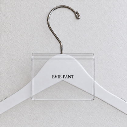 Clear acrylic hanger sign clip with soft edge reflections, resting on a white wooden hanger, with example EVIE PANT print