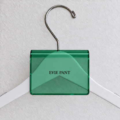 Green transparent acrylic hanger sign clip with soft edge reflections, resting on a white wooden hanger, with example EVIE PANT print