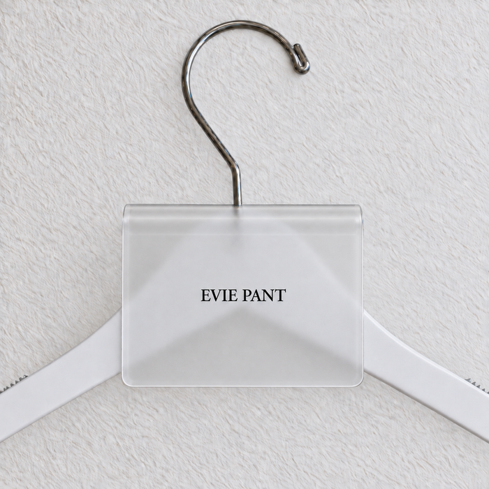Clear Matte acrylic hanger sign clip with soft edge reflections, resting on a white wooden hanger, with example EVIE PANT print