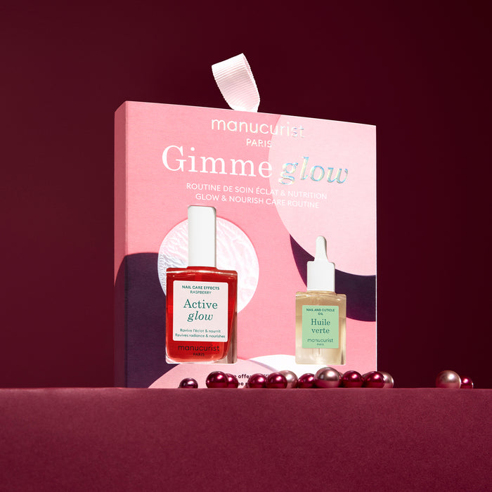 A pink box labeled 5min' Glow Manicure by Manucurist stands upright, holding two nail treatments—one red and one pale green—against a burgundy background with scattered pearls.
