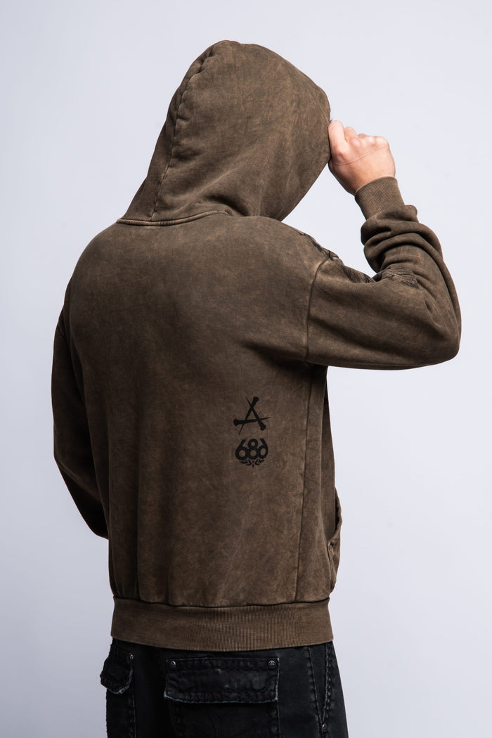 A person faces away from the camera wearing a 686 Affliction Natural Rot Pullover Hoody with the hood up, showing black graphics on the back and holding the hood‚Äôs edge with one hand.