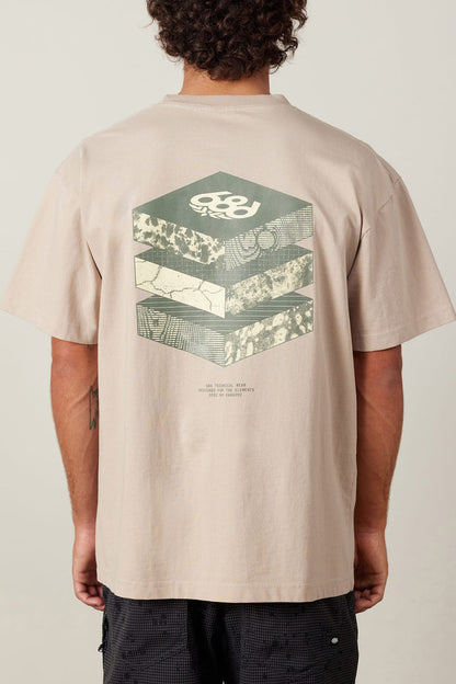 A person wears the 686 Elements Relaxed S/S Tee by 686, a beige men‚Äôs t-shirt made from 100% cotton, featuring geometric hexagonal graphics and layered abstract patterns with a small text section on the back.