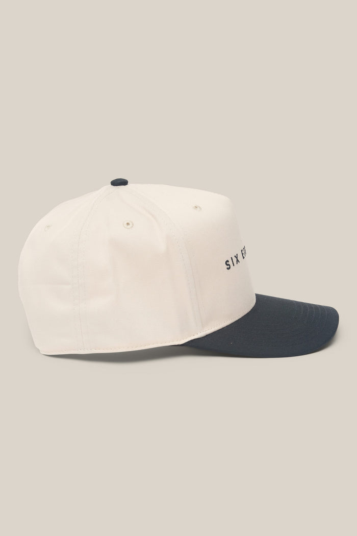 A white 686 High-Pro Ses Two Tone Structured 5 Panel Hat made of cotton with a black brim is shown from the side. This men's hat by 686 features small ventilation holes and has the partially visible text "SIX E" on the front.