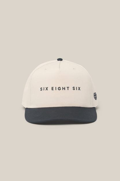 Introducing the 686 High-Pro Ses Two Tone Structured 5 Panel Hat by 686—a beige cotton men’s hat with a black brim and “SIX EIGHT SIX” embroidered in black on the front, blending classic style and everyday comfort.