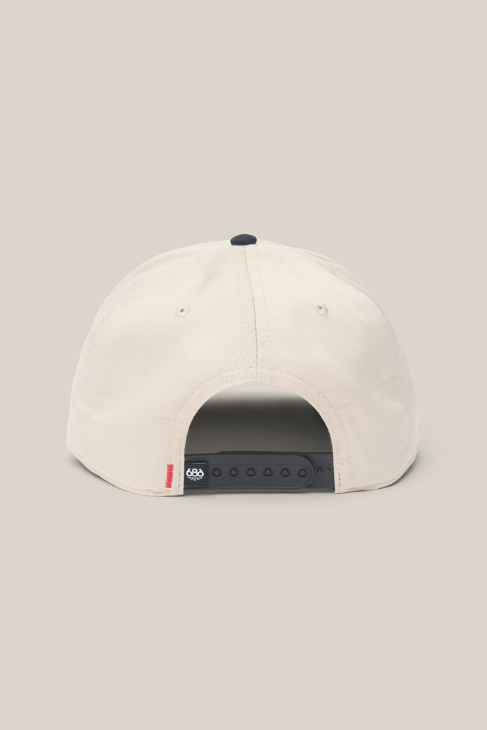 The 686 High-Pro Ses Two Tone Structured 5 Panel Hat by 686 is shown in beige cotton from the back, featuring a black adjustable snapback closure and a small red tag on the bottom left side.