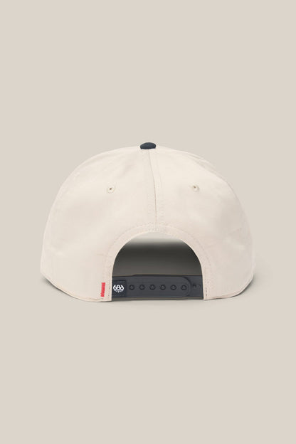 The 686 High-Pro Ses Two Tone Structured 5 Panel Hat by 686 is shown in beige cotton from the back, featuring a black adjustable snapback closure and a small red tag on the bottom left side.