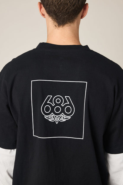 A person shown from behind wears the 686 Wordmark Relaxed 2fer LS Tee, a black 100% cotton men‚Äôs t-shirt by 686, featuring a white outlined square with the 686 logo and graphic design on the back, complementing their short brown hair.