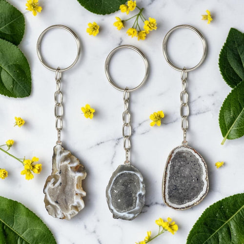 Three geode keychains on a marble surface with green leaves and yellow flowers.