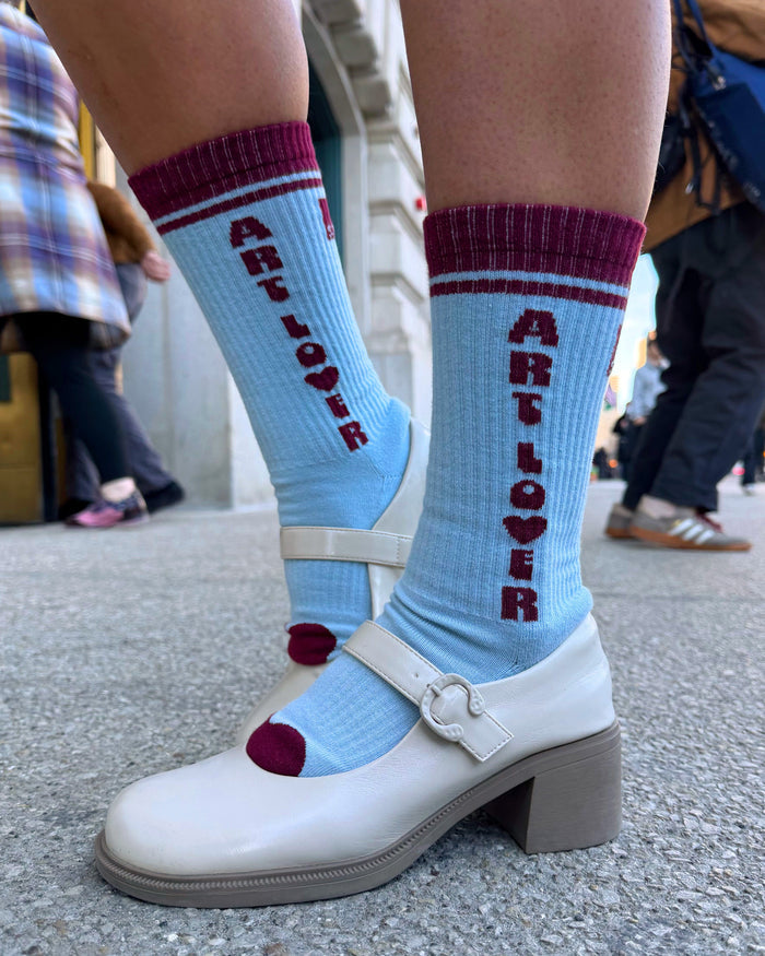 Person wearing light blue socks with 'ARTLOVER' text and white shoes on a street.