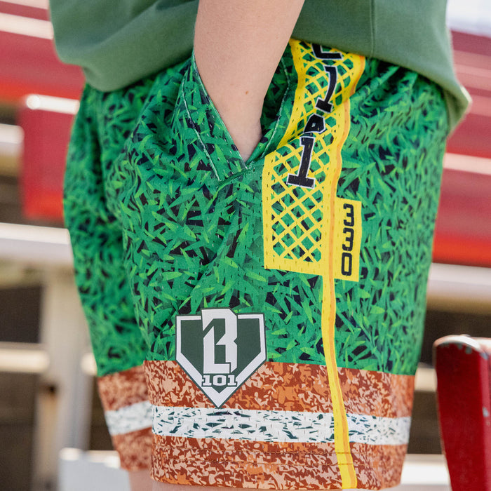 Close up of green grass print mesh shorts with yellow foul pole side stripe BL101 logo patch and brown marbled hem