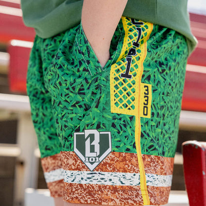 Close up of green grass print mesh shorts with yellow foul pole side stripe BL101 logo patch and brown marbled hem