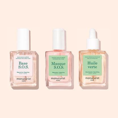 Three square bottles from Manucurist’s Basic Routine - Damaged Nails set are displayed with pastel backgrounds and white caps—one topped with a dropper. The labels read: Base S.O.S., Masque S.O.S., and Huile Verte, each formulated to strengthen and repair brittle nails.