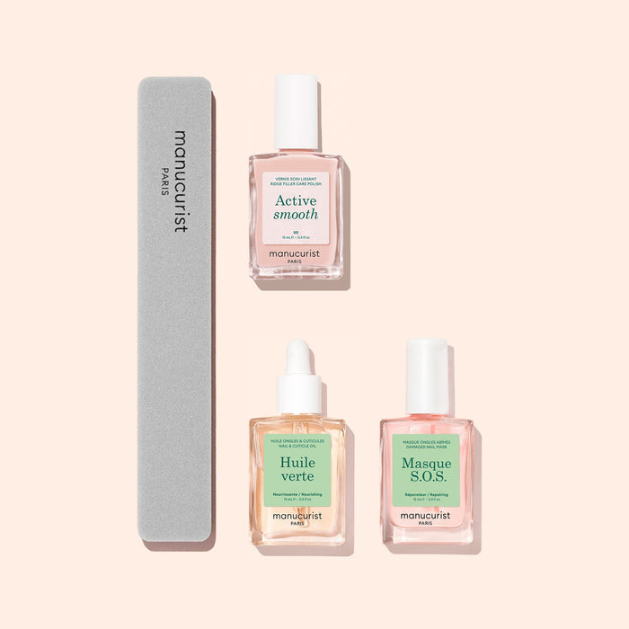 Three glass bottles from the Manucurist Basic Routine - Ridged Nails set, along with a gray nail file, are arranged neatly on a light peach background—perfect for your daily nail care ritual. The bottles include Active Smooth, Huile Verte (a nourishing cuticle oil), and Masque S.O.S., all specially formulated to restore strength to ridged nails and promote overall nail health.