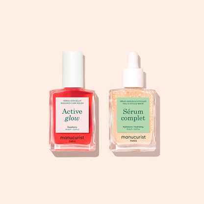 Two bottles from Manucurist’s Basic Routine - Sensitive Nails—a vibrant red Active Glow nail polish with a white cap and a clear Serum Complet cuticle serum with a dropper—are beautifully arranged on a light peach background, offering the perfect duo for nail care and moisturized nails.