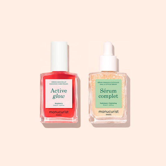 Two bottles from Manucurist’s Basic Routine - Sensitive Nails—a vibrant red Active Glow nail polish with a white cap and a clear Serum Complet cuticle serum with a dropper—are beautifully arranged on a light peach background, offering the perfect duo for nail care and moisturized nails.