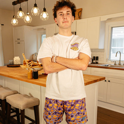 Male model wearing BL101 purple PB&J print mesh shorts and a white BL101 tee in a kitchen setting.