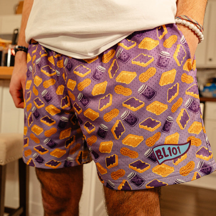 Close-up front view of BL101 purple PB&J print mesh shorts on a male model, showing the all-over print and BL101 logo.