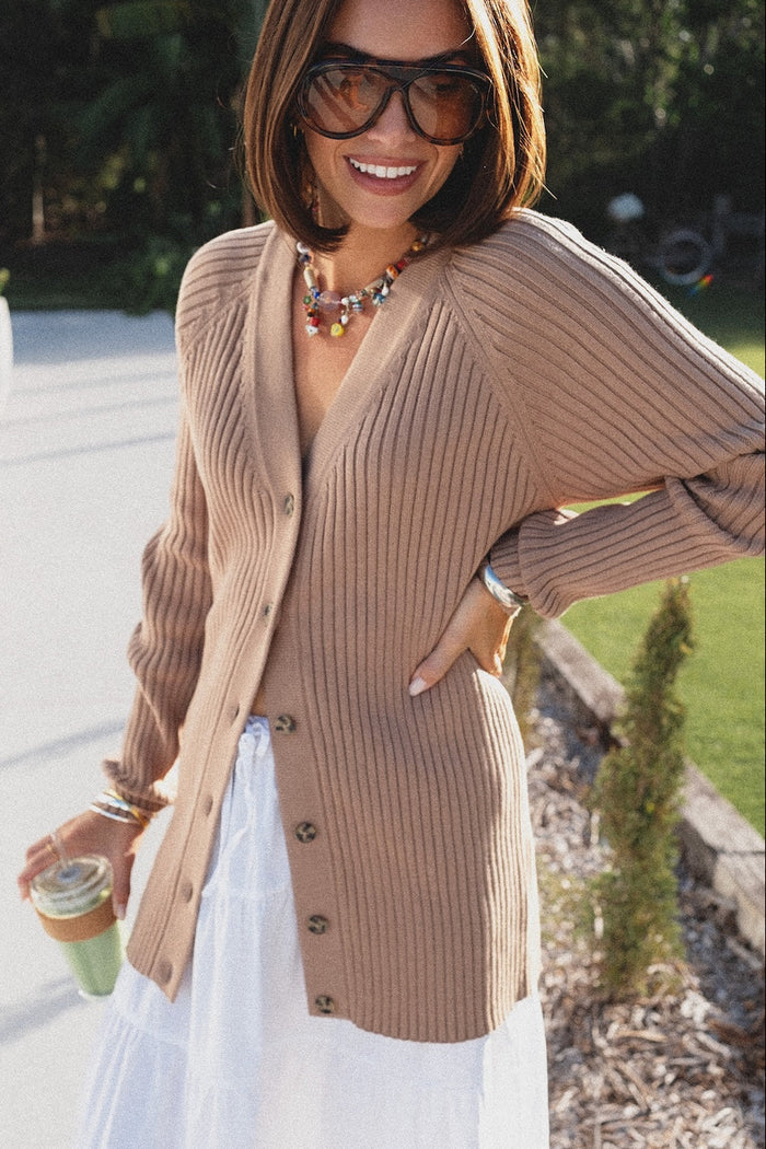Woman wearing a beige cardigan and sunglasses outdoors