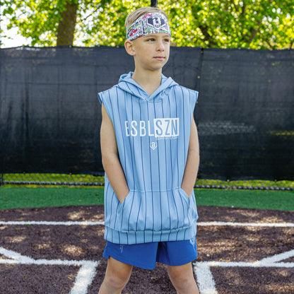 Child wearing a light blue sleeveless hoodie with 'BSBLSZN' branding on a baseball field.