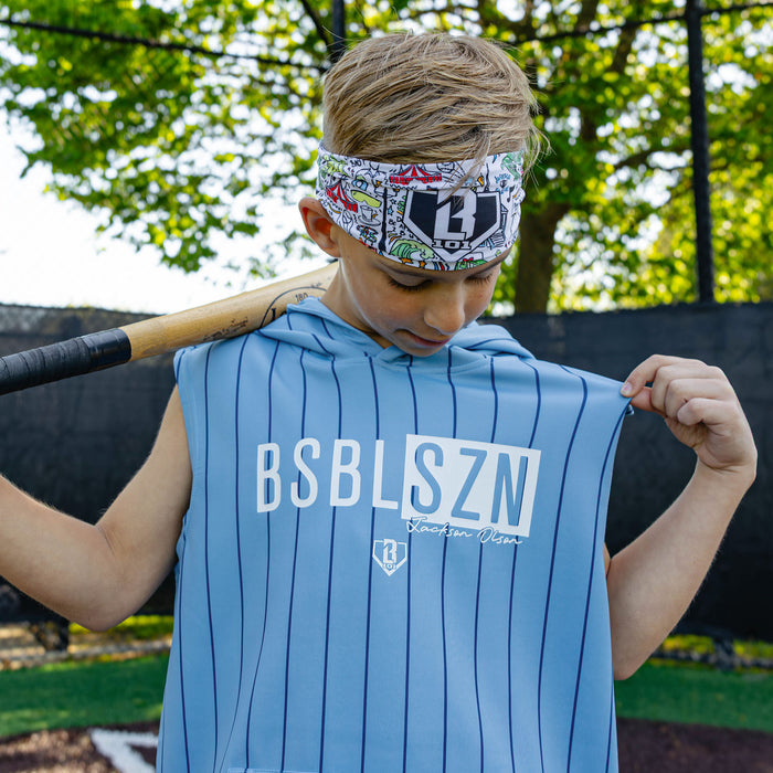 Youth player holding a bat over his shoulder wearing the light blue pinstripe Jackson Olson x BL101 BSBL-SZN Short Sleeve Hoodie V3 with Jackson Olson graphic headband