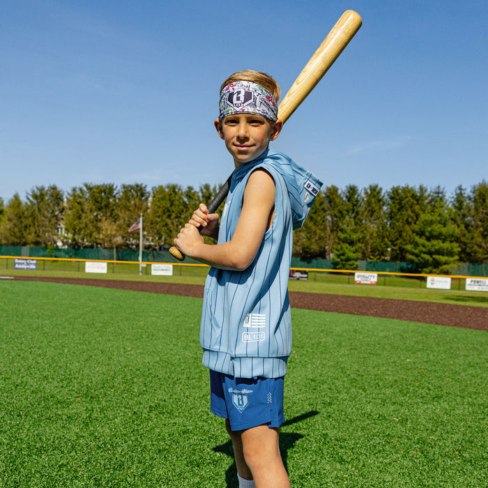 Youth player on a baseball field holding a bat over his shoulder, wearing the light blue pinstripe BSBL-SZN Short Sleeve Hoodie V3 with Jackson Olson graphic headband and blue shorts