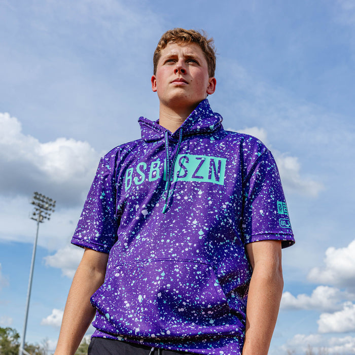 Youth model wearing splatter purple and teal BSBL-SZN youth short sleeve hoodie