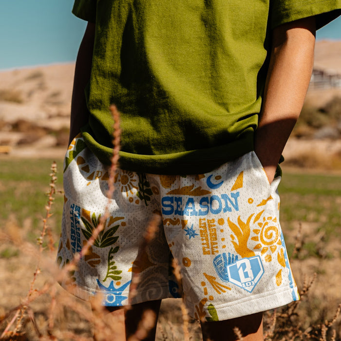 Person wearing a green shirt and white, orange and blue desert patterned shorts in an outdoor setting