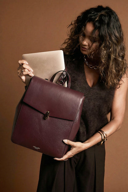 Female model putting a laptop in the back laptop pocket of Casey Black 
Cherry faux leather Laptop Backpack