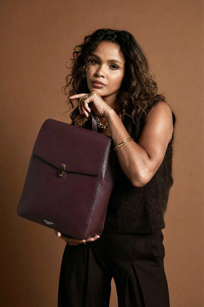 Female model holding Casey Black Cherry faux leather Laptop Backpack by the top reptile printed grab handle