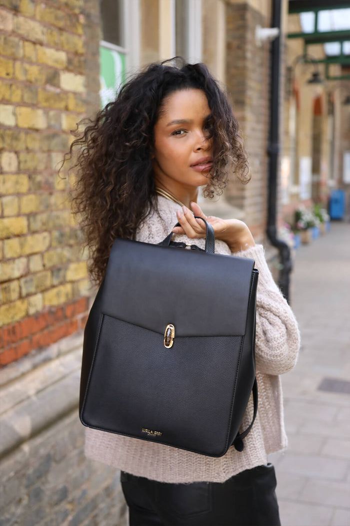 Female model holding Casey Black faux leather Laptop Backpack behind her by the top reptile printed grab handle
