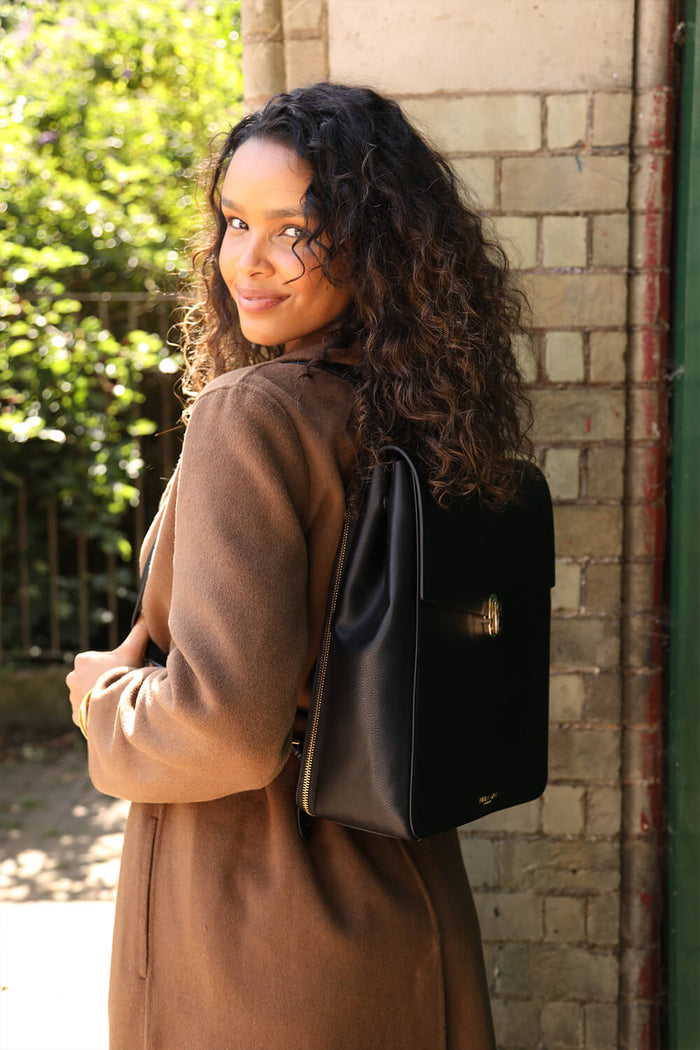 Female model wearing Casey Black faux leather Laptop Backpack using both straps over her shoulders showing the front of the backpack