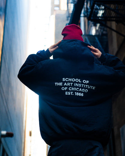 Person wearing a black zip sweater with 'School of the Art Institute of Chicago' text, standing in an urban setting.