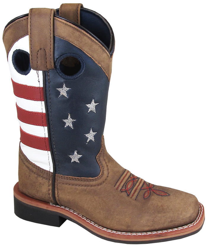 A child's square-toe boot with a light brown distressed foot and stars and stripes pattern on top, predominantly red, white, and blue, indicating an American flag design.