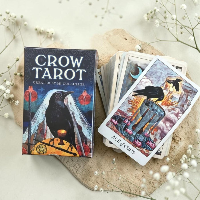 Crow Tarot card set with deck and box on a light surface with flowers.