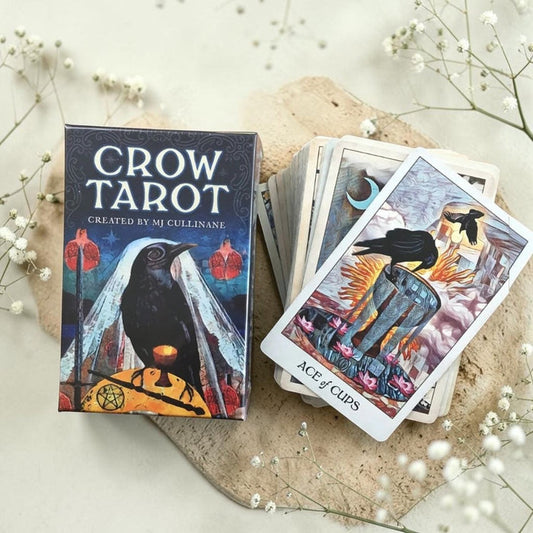 Crow Tarot card set with deck and box on a light surface with flowers.