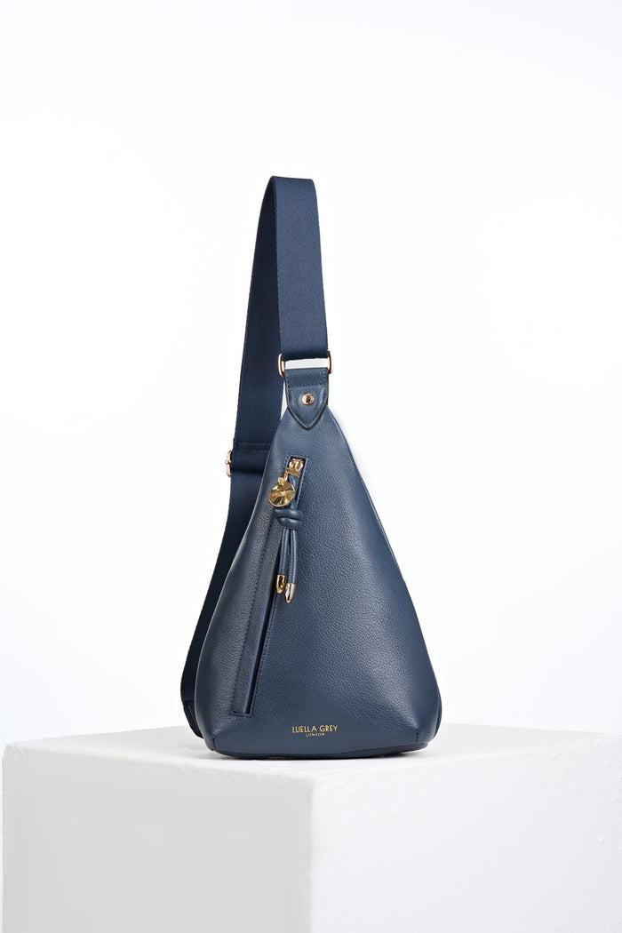 Front view of Darla Denim Blue faux leather Sling Crossbody with Clissold Knot charm zip pull closure
