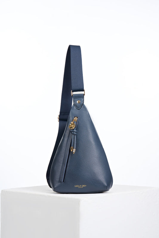 Front view of Darla Denim Blue faux leather Sling Crossbody with Clissold Knot charm zip pull closure