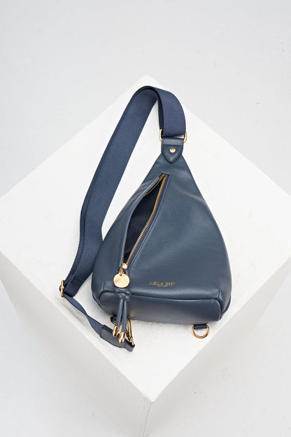 overhead view of Darla Denim Blue faux leather Sling Crossbody laying flat on the table with the front pocket unzipped and open