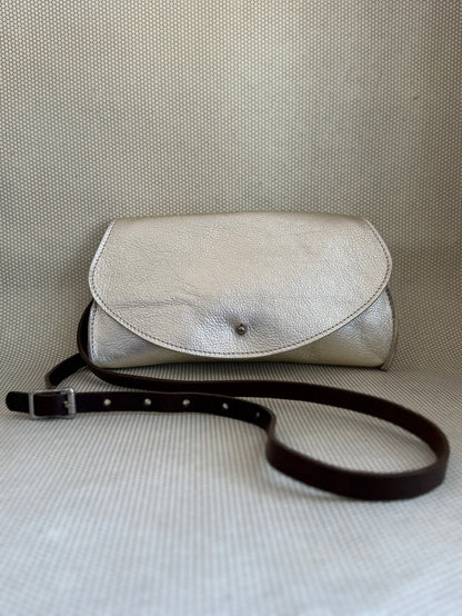 silver Dean leather clutch bag on a textured surface with strap.